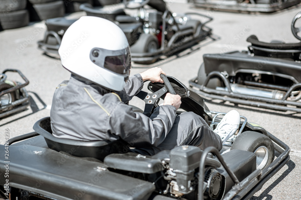 Portrait of a male racer in sportswear and protecive helmet sitting in the go-kart on the track outd