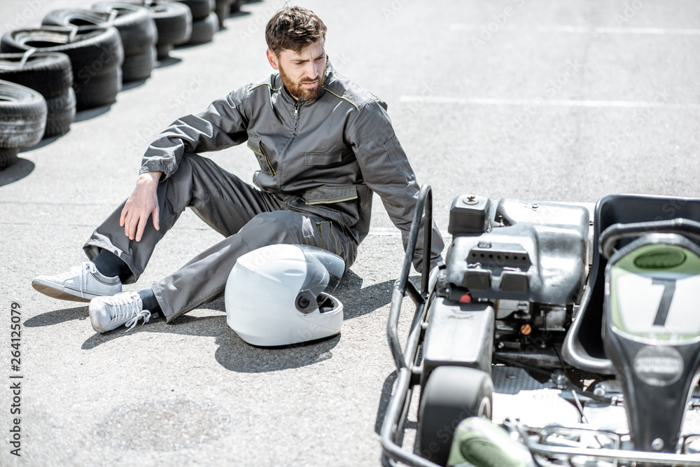 Despair racer in sportswear feeling sad lying on the track near the kart as a loser outdoors