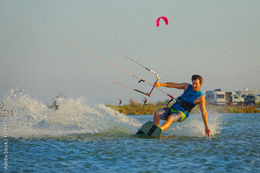 Cool male kitesurfer drags his hand along the calm surface of the blue ocean.