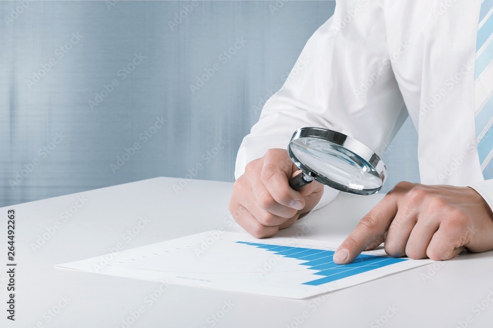 Business analytics and statistics. Businessman with report using a magnifying glass.