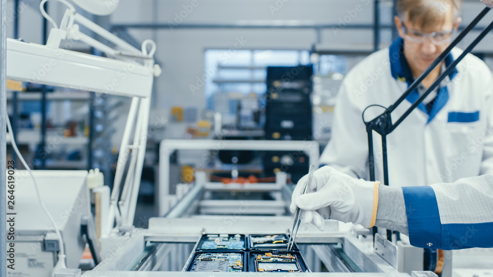 Shot of an Electronics Factory Workers Assembling Circuit Boards by Hand While it Stands on the Asse