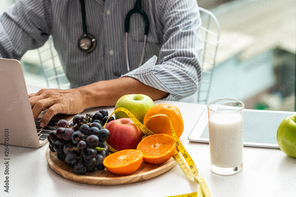 Senior male nutritionist doctor working on desk with healthy food fruits and milk on table in the ho