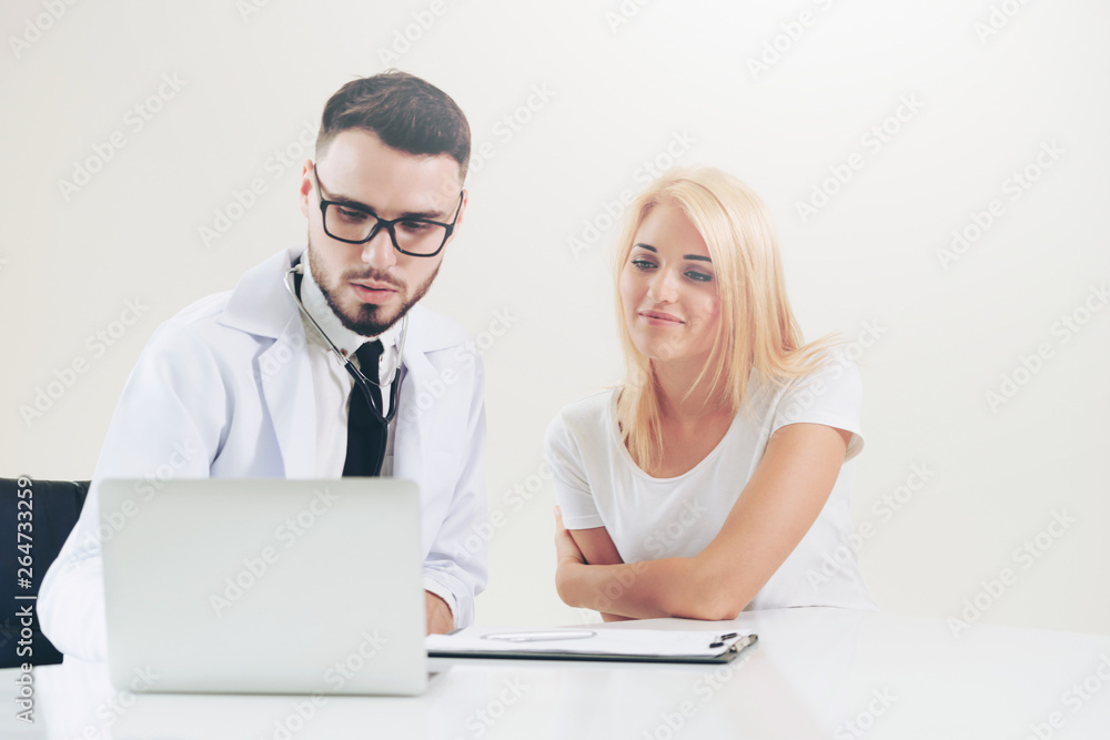 Male doctor talks to female patient in hospital office while looking at the patients health data on 