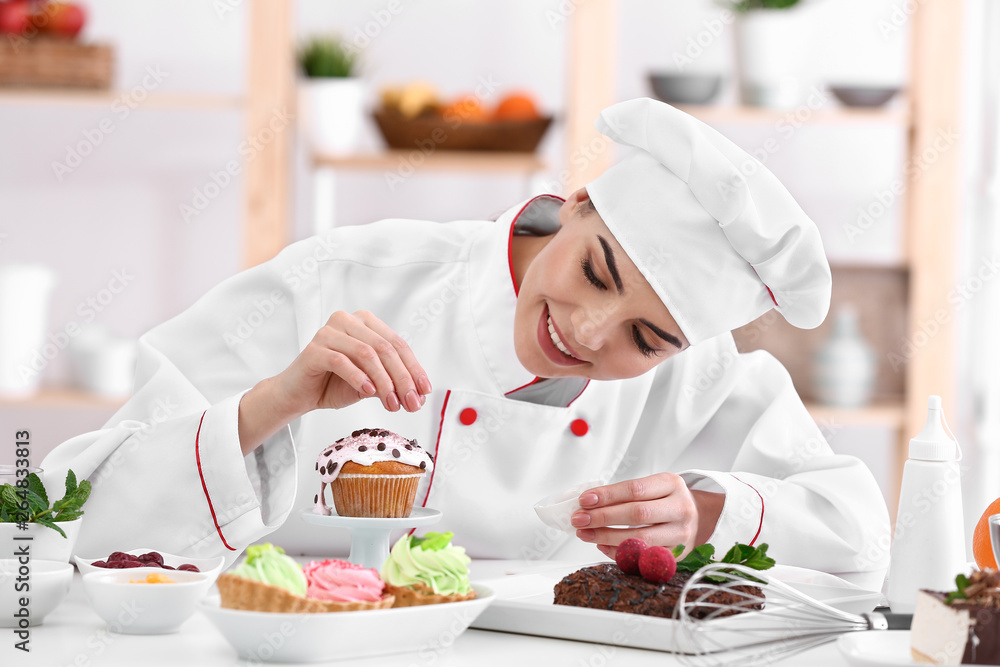 Young female confectioner decorating cupcake in kitchen