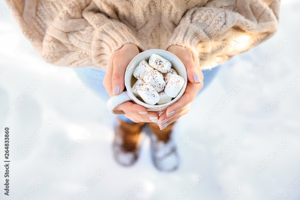 Woman holding cup of hot cacao with marshmallows on winter day