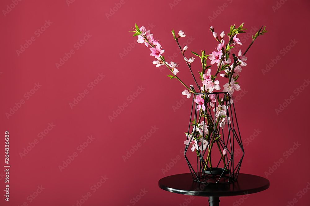 Vase with beautiful blossoming branches on table against color background