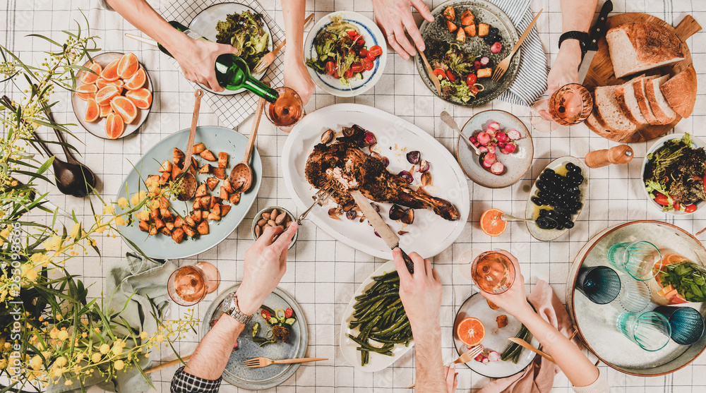 Family or friends gathering dinner. Flat-lay of hands of people eating roasted lamb shoulder, salads