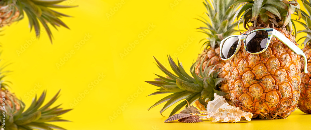 Creative pineapple looking up with sunglasses and shell isolated on yellow background, summer vacati