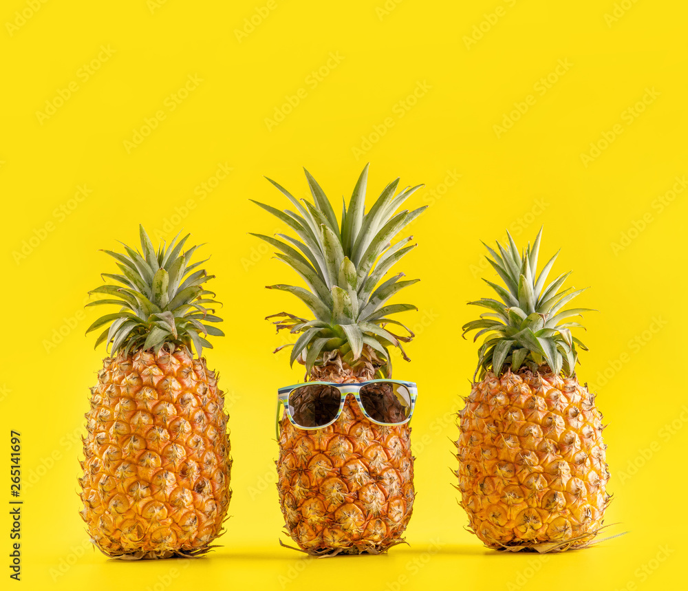 Creative pineapple looking up with sunglasses and shell isolated on yellow background, summer vacati