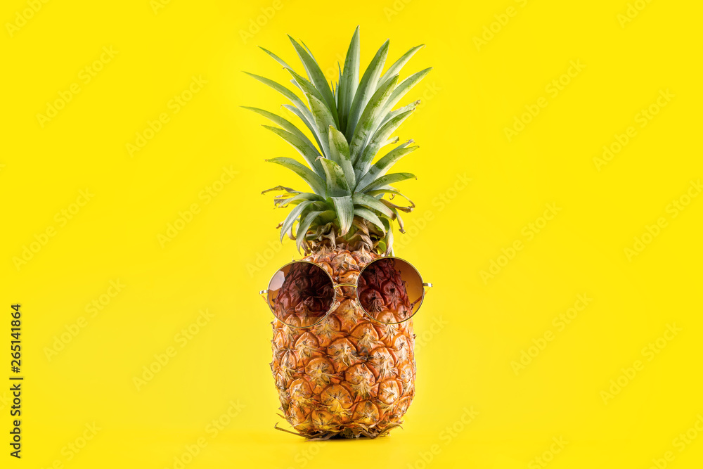 Creative pineapple looking up with sunglasses and shell isolated on yellow background, summer vacati