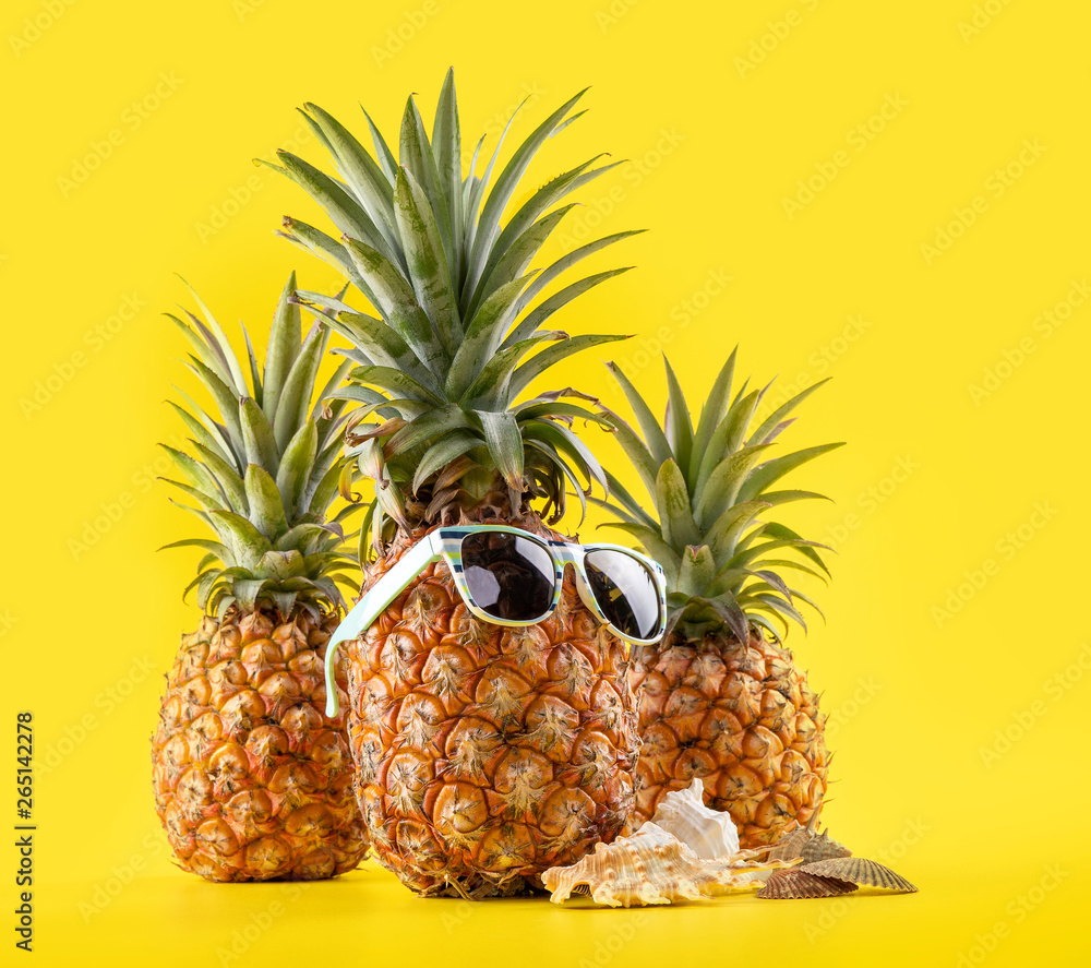 Creative pineapple looking up with sunglasses and shell isolated on yellow background, summer vacati