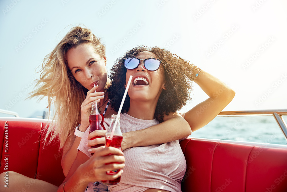 Laughing friends sitting on a boat enjoying drinks during vacati