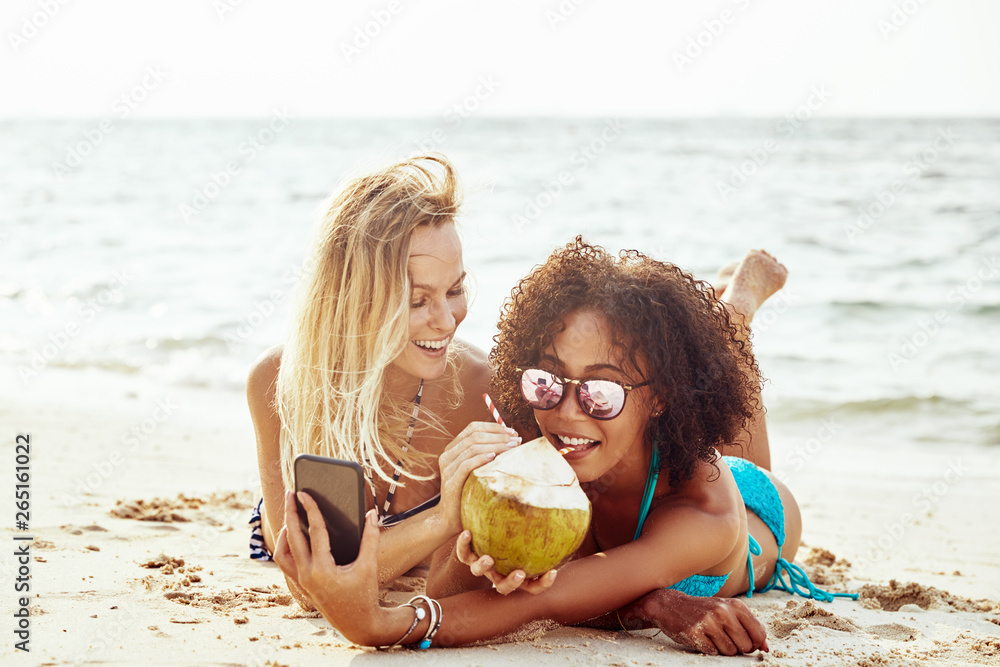 Suntanning friends taking selfies together on a tropical beach