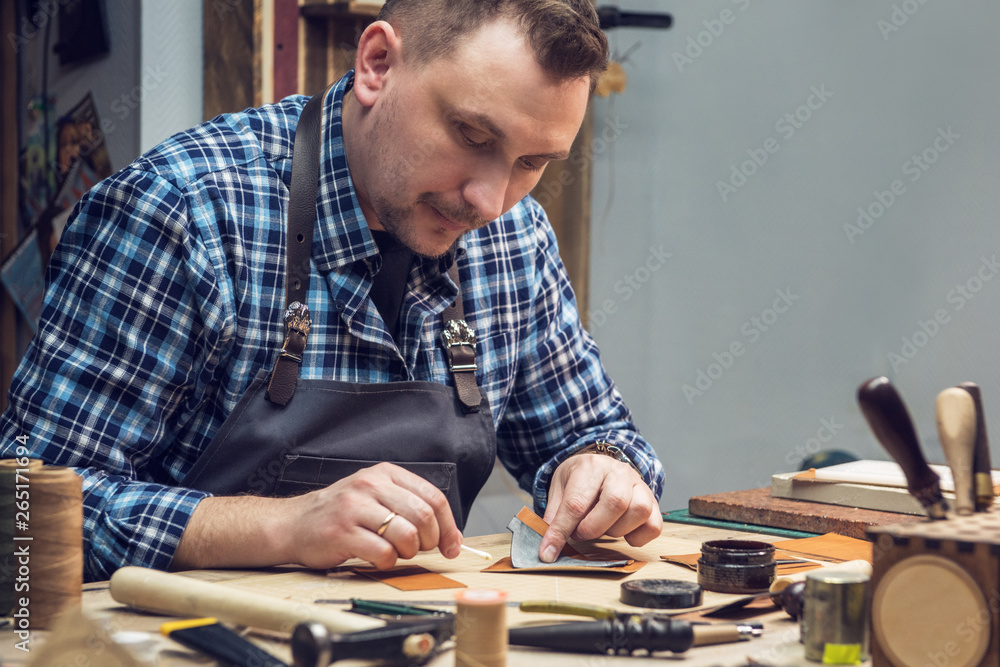 Man working with leather textile at a workshop. Concept of handmade craft production of leather good