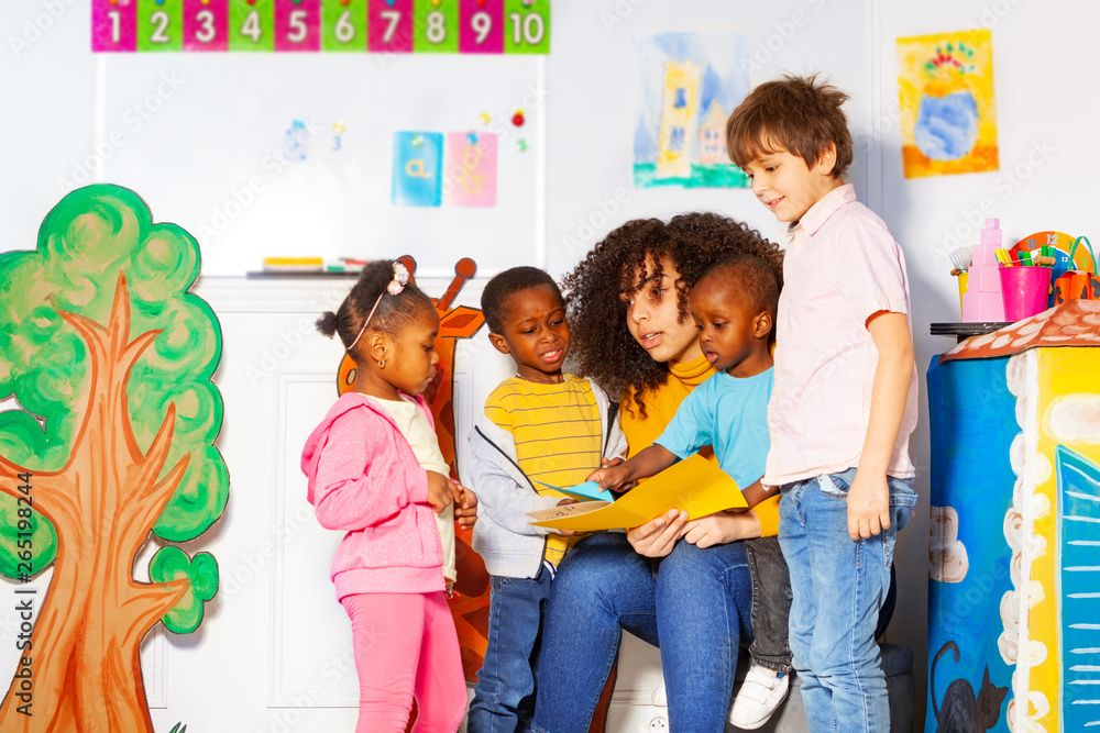 Group of kids reading book with teacher in nursery