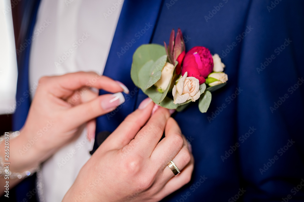 Brides hands pinning a small boutonniere to a jacket for the groom. Floral traditional decoration f