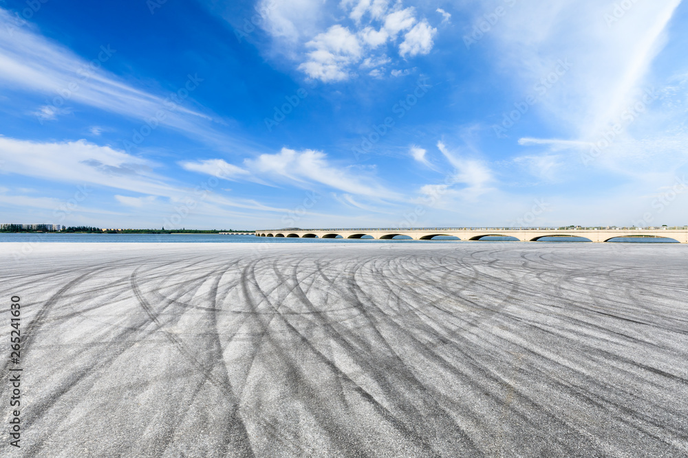 Asphalt race track ground and lake with bridge under blue sky