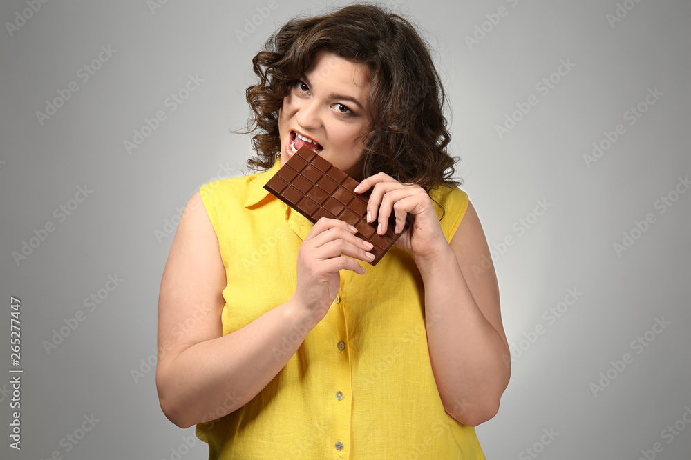 Overweight woman with chocolate on grey background