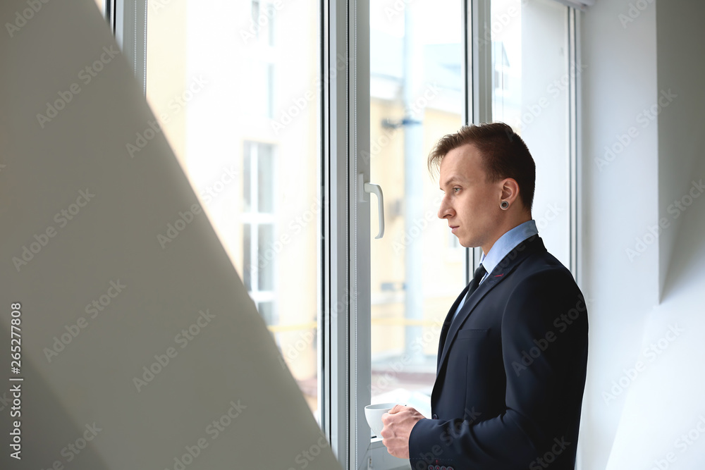 Handsome stylish businessman with cup of coffee near window