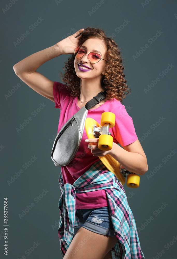 Stylish young woman with skateboard on grey background