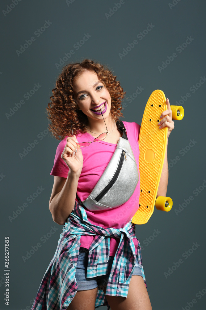 Stylish young woman with skateboard on grey background