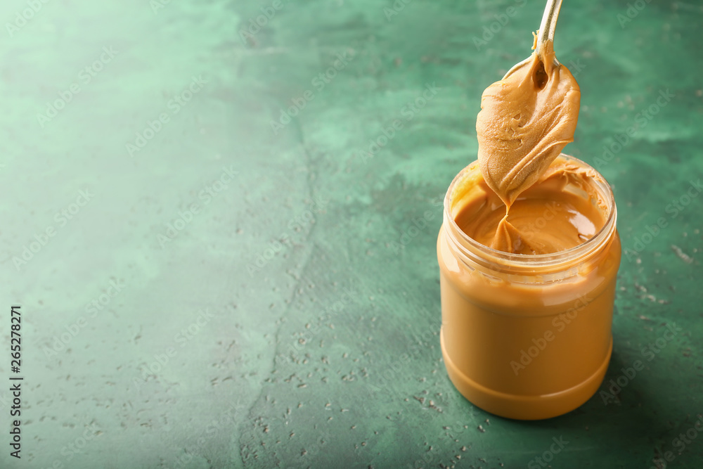 Taking of tasty peanut butter from jar on color background