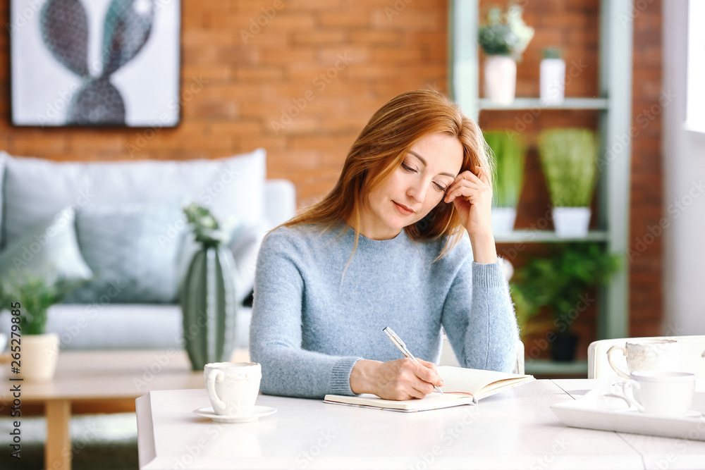 Portrait of mature woman writing in notebook at home