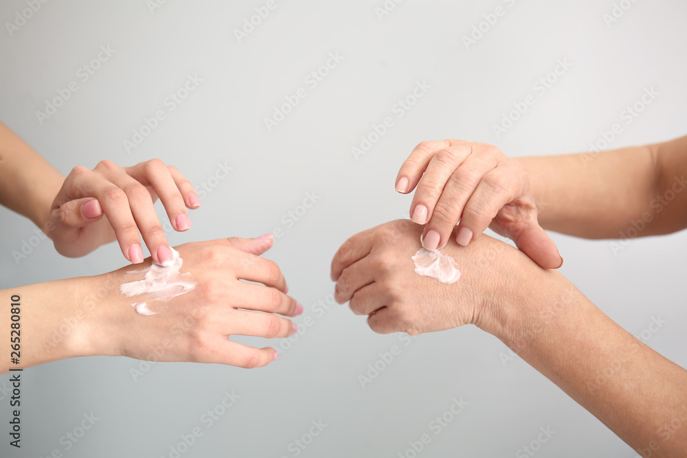 Young and mature women applying hand cream on light background