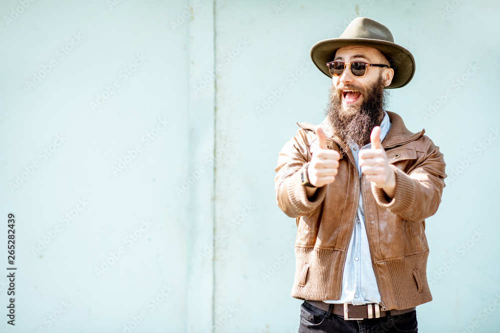 Portrait of a stylish bearded man showing ok sign on the light turquoise background outdoors