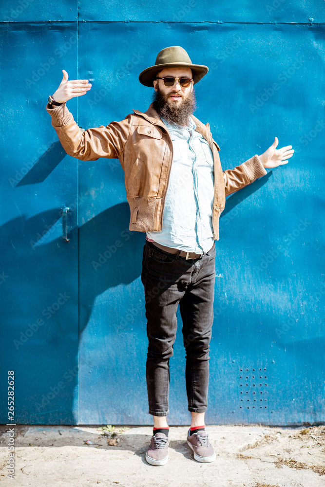 Full body portrait of a stylish man posing on the blue metal wall background outdoors