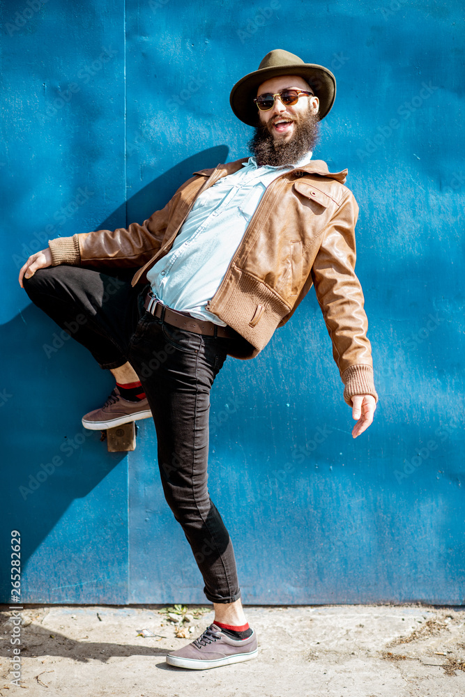 Full body portrait of a stylish man posing on the blue metal wall background outdoors