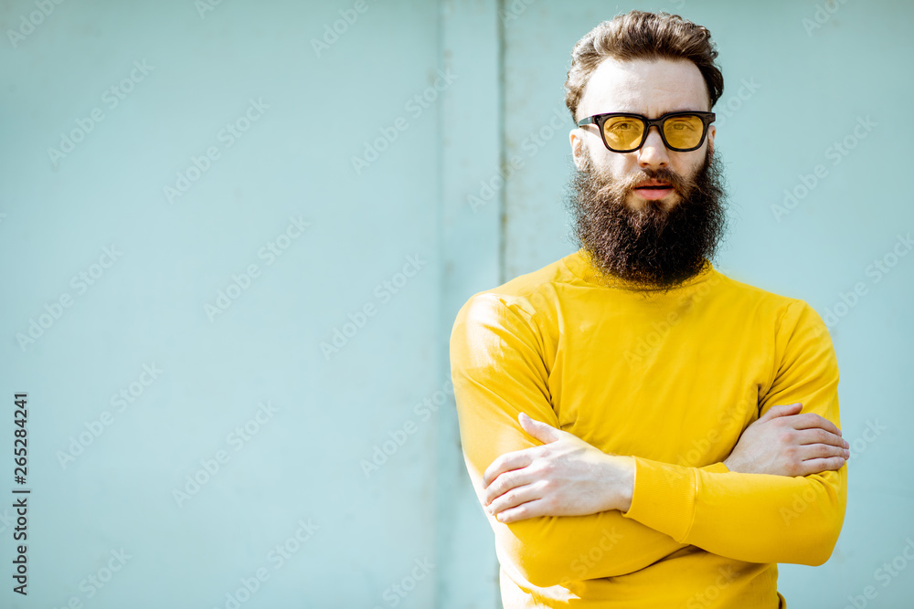 Portrait of a confident stylish bearded man in yellow sweater on the turquoise background outdoors