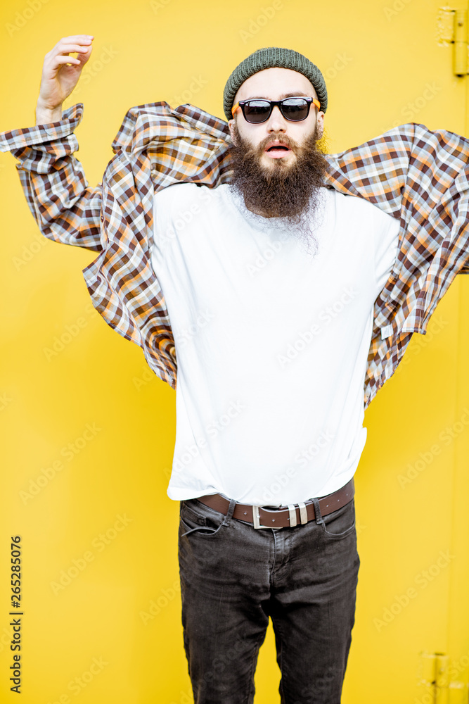 Portrait of a cool stylish man in shirt and hat posing on the bright yellow background