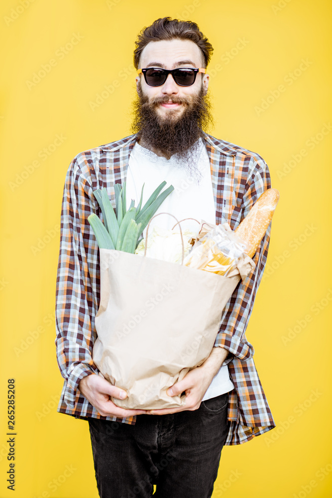 一个留着胡子的男人站在亮黄色的背上，手里拿着装满食物的购物纸袋的肖像