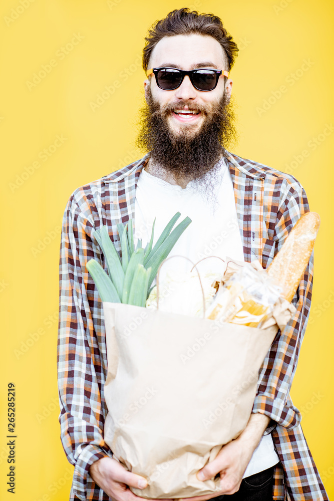 一个留着胡子的男人站在亮黄色的背上，手里拿着装满食物的购物纸袋的肖像