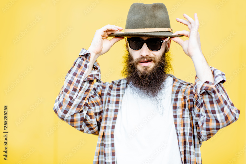 Portrait of a cool stylish man in shirt and hat posing on the bright yellow background