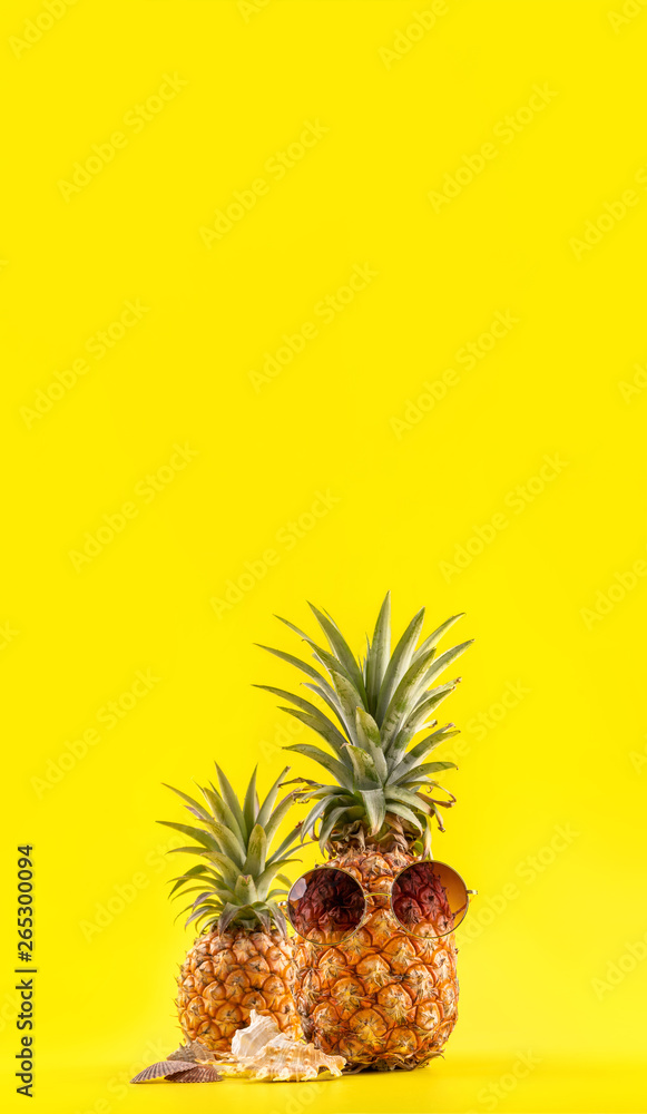 Creative pineapple looking up with sunglasses and shell isolated on yellow background, summer vacati