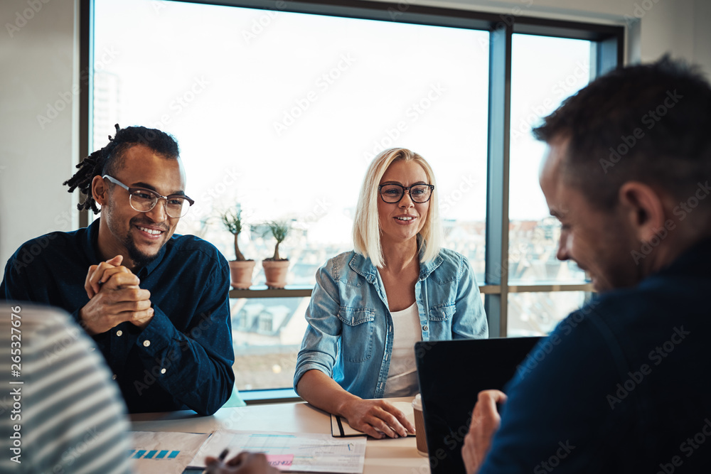 Smiling young colleagues meeting around a table in an office