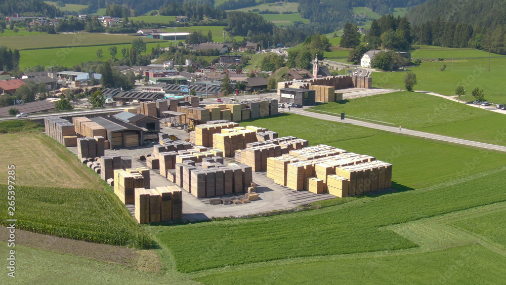 AERIAL: Cars drive towards the village and past a large sawmill in sunny Austria