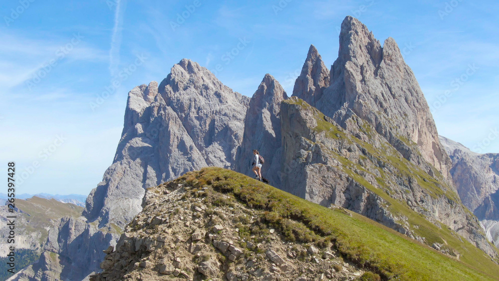 AERIAL: Flying along tourist girl hiking up towards the mountaintop with puppy.