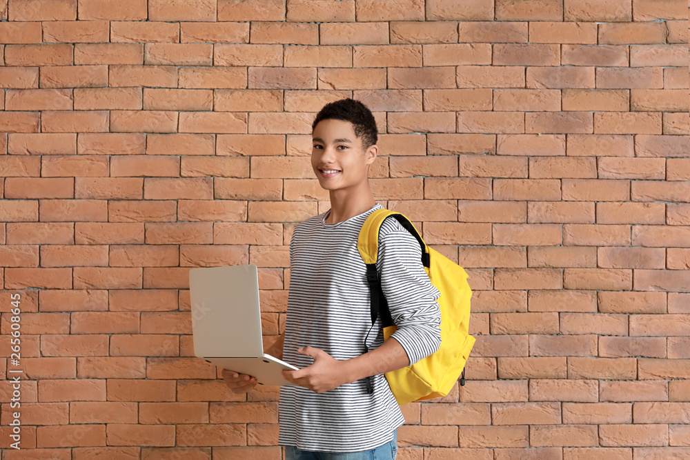 African-American teenage boy with laptop near brick wall