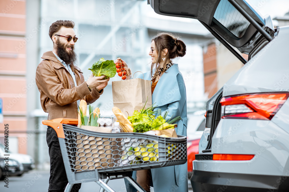 年轻时尚的情侣带着装满新鲜食物的购物车，出门就把产品装进车里