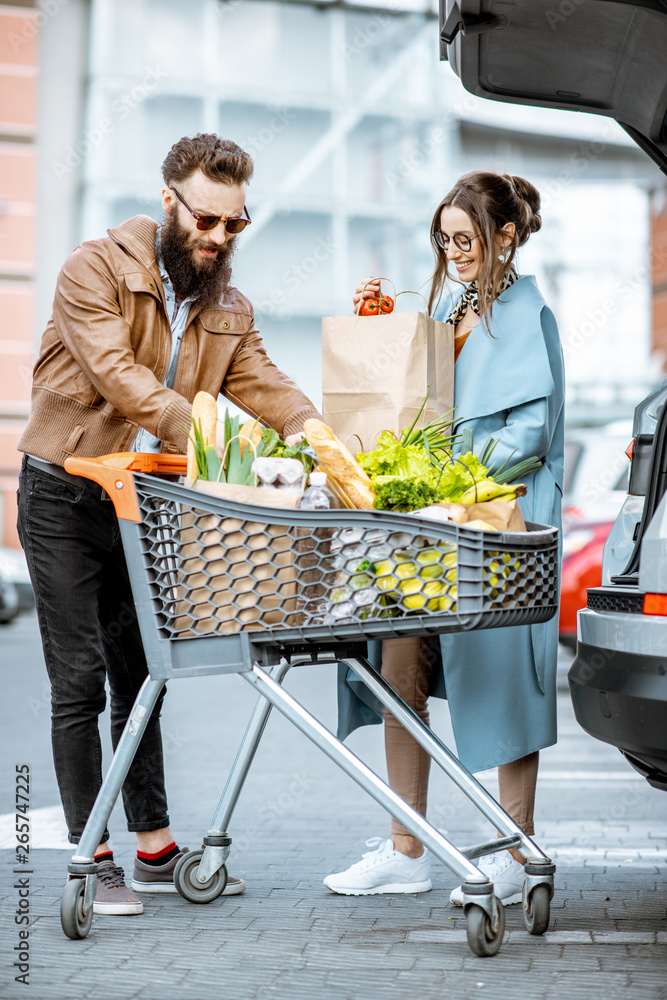 年轻时尚的夫妇带着装满新鲜食物的购物车，出门就把产品装进车里