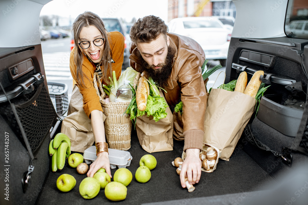 Young couple packing shopping bags with fresh food into the car trunk, view from the vehicle interio