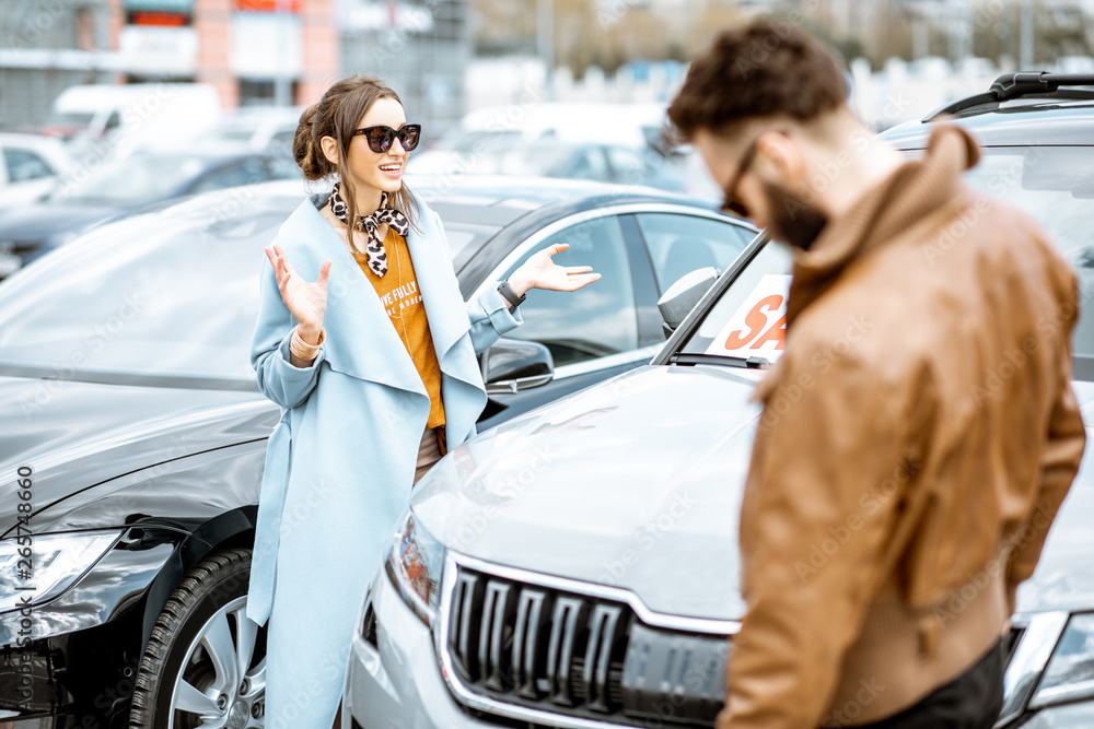 Young stylish couple choosing luxury car to buy on the open ground of the dealership