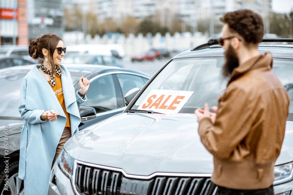 Young stylish couple choosing luxury car to buy on the open ground of the dealership