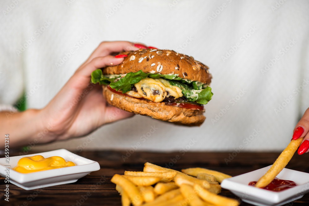 Womans hand dipping french fries in barbecue sauce. Delicious fresh burger with tomato and cheese. 