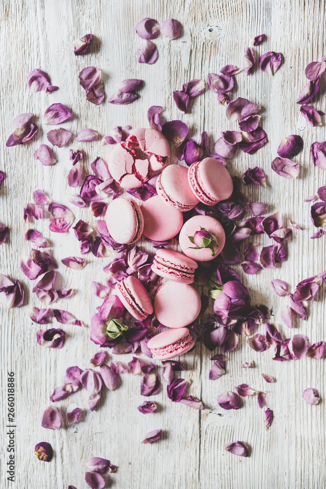 木质背景上平放的甜粉色马卡龙饼干、玫瑰花蕾和花瓣，俯视图，ve