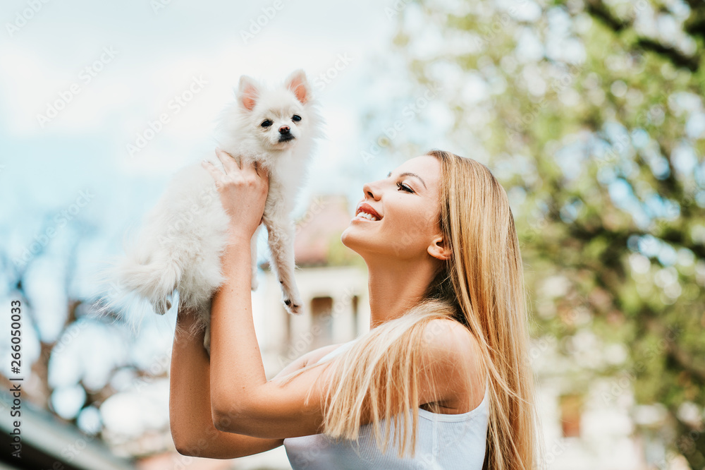 Outdoor portrait of happy young woman holding white pomeranian spitz puppy