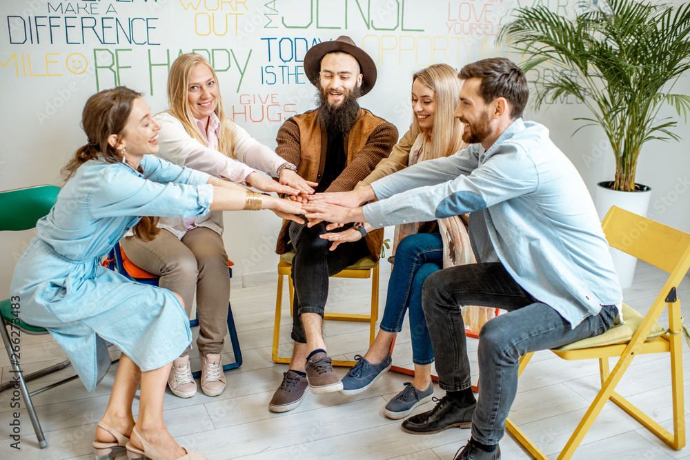 Group of happy people keeping hands together, sitting in a circle during the psychological therapy i